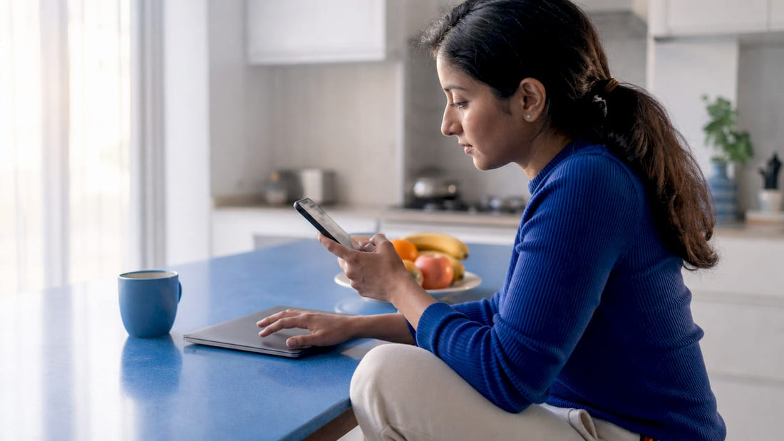 Woman using phone and laptop at home office desk